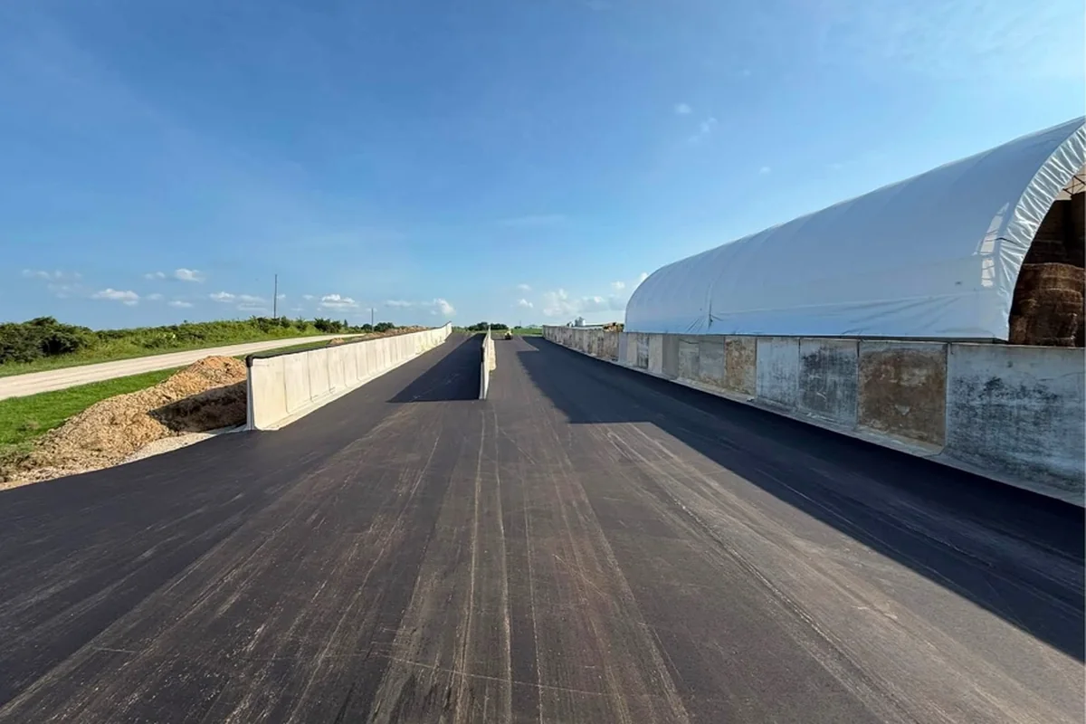Long asphalt feed bunker floor running between concrete walls beside a hoop building