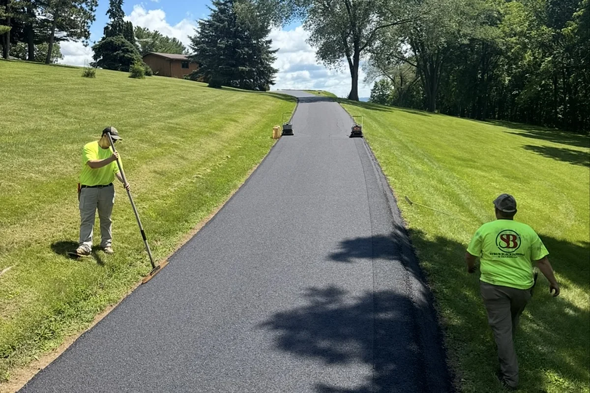 Two Strub crew members finishing the edges of a freshly paved rural lane
