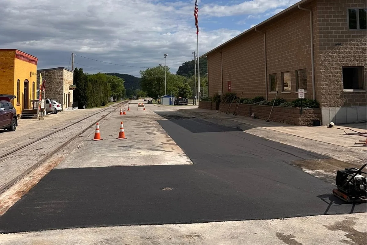 Fresh asphalt patch laid across a downtown street beside a brick building and flagpole