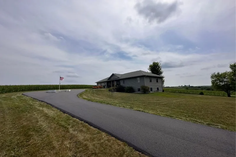 Long curved asphalt driveway climbing to a hilltop home beside a cornfield