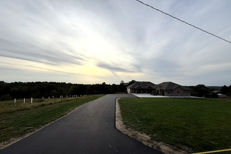Long new asphalt driveway running up to a rural home at sunset