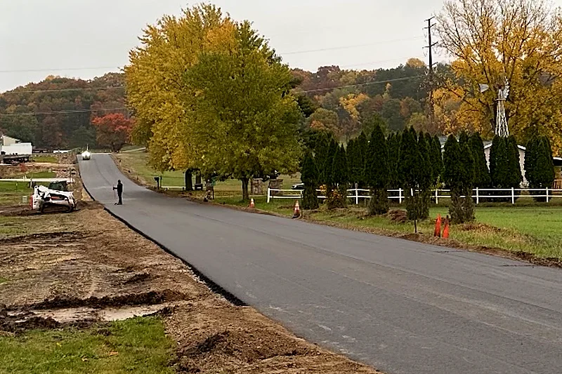 Freshly paved rural road running past a farm on an overcast fall day