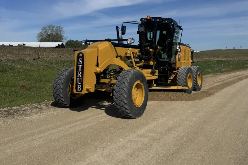 Strub motor grader shaping a gravel road through open farm country