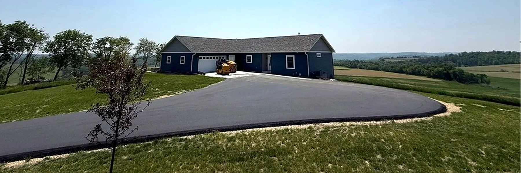 Wide asphalt circle drive wrapping around a rural home on a hilltop