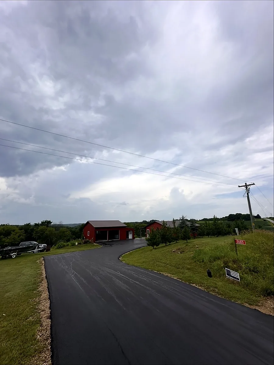 Drive curving past a red barn under a stormy sky