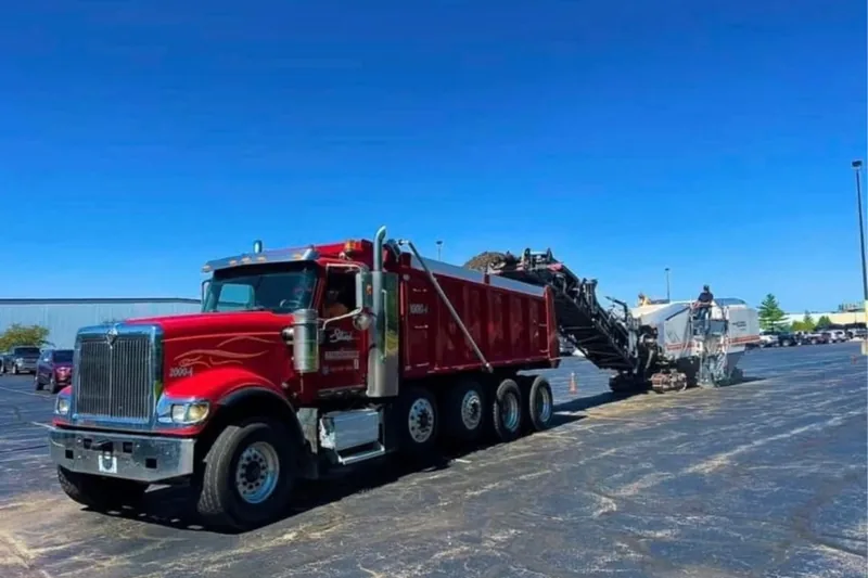 Strub dump truck running alongside a milling machine resurfacing a commercial lot
