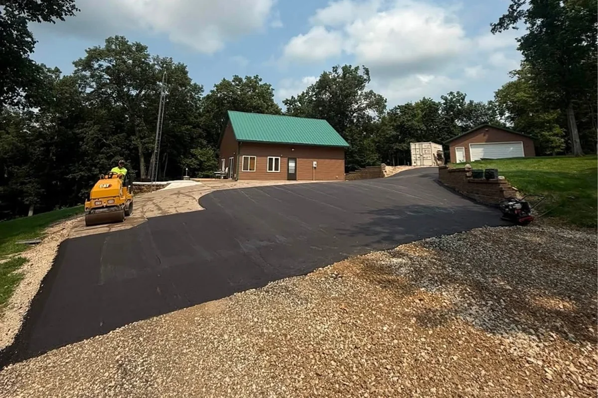 Freshly paved asphalt driveway sweeping past a rural home and shop building