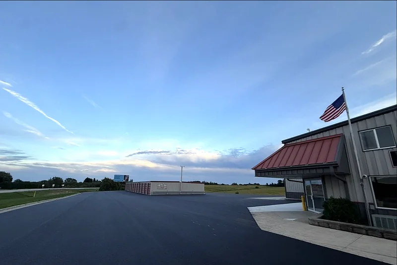 Freshly paved commercial lot at dusk beside a business entrance, with storage units and open country behind it