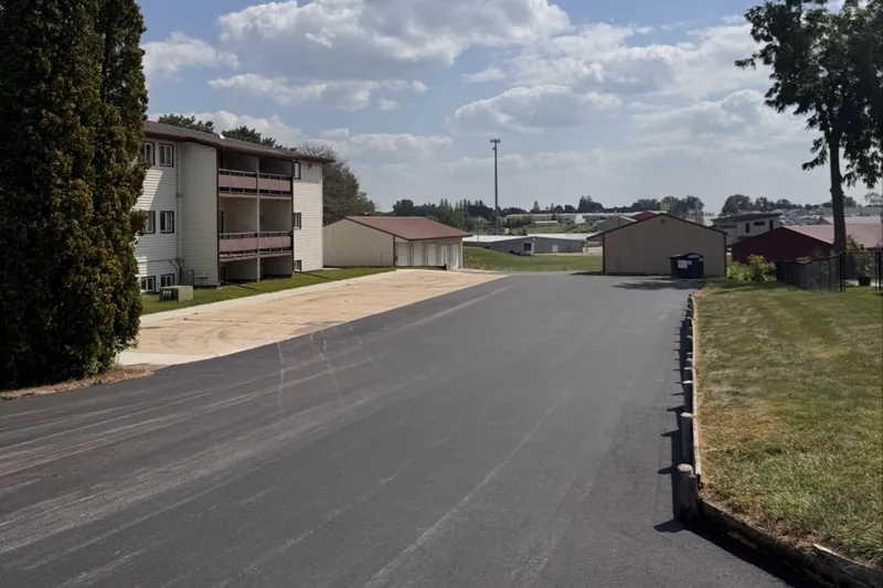 Newly paved street running past an apartment building and outbuildings